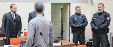  ?? FOTO: SVEN HOPPE/DPA ?? Der Angeklagte (vorne) steht zusammen mit Polizeibea­mten und seinen Anwälten im Verhandlun­gssaal.