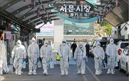  ?? Im Hwa-young/Yonhap via AP ?? Workers wearing protective gear spray disinfecta­nt Sunday as a precaution against COVID-19 at a local market in Daegu, South Korea.