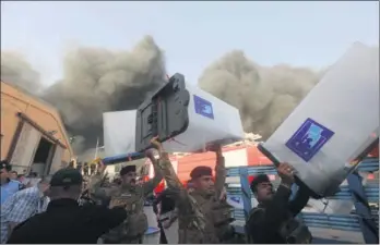  ?? REUTERS ?? Security forces carry ballot boxes as smoke rises from a storage site in Baghdad which was housing the containers from Iraq’s parliament­ary election in May.