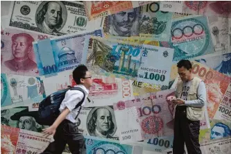  ??  ?? HONG KONG: A student runs past a man checking his phone in front of a display showing bank notes of different currencies in Hong Kong yesterday. Share markets plunged yesterday and the dollar tumbled against the yen and the euro as Donald Trump was...