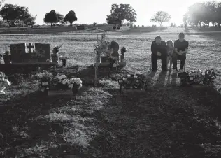  ??  ?? “The only way I could get them back is with a time machine,” Holcombe says as he sits with his children, Evelyn and Philip, at the graves of their family members.