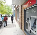  ?? FILE PHOTO BY DAN HENRY ?? Pedestrian­s walk past a Synovus ATM on Market Street in downtown Chattanoog­a. In 2018, Cohutta Bank will be renamed Synovus, which was rated the No. 1 bank by the Reputation Institute.