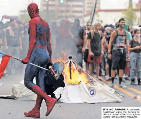  ??  ?? IT’S NO PARADE: A costumed Spider-Man walks past burning debris at a protest in San Juan against Puerto Rico’s austerity measures.