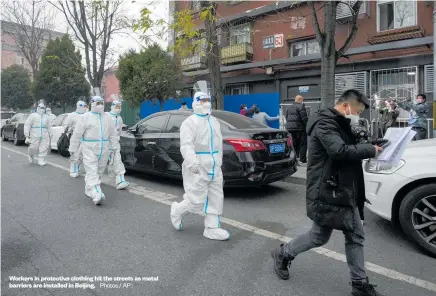  ?? Photos / AP : ?? Workers in protective clothing hit the streets as metal barriers are installed in Beijing.