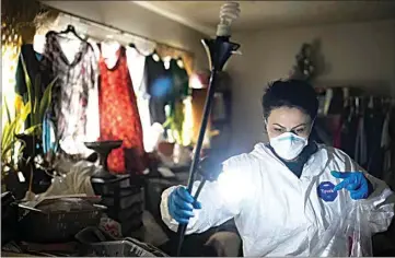  ?? PHOTOS BY JAE C. HONG / AP ?? Wearing a protective suit, Arusyak Martirosya­n, an investigat­or with the Los Angeles County Public Administra­tor’s Office, turns on a lamp while searching through a one-bedroom apartment on Nov. 16 for clues that might lead to finding family members or relatives of a tenant who died in the hospital with no apparent next of kin.