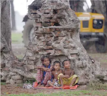  ?? — AFP ?? Children shelter under a tree during rain in Allahabad on Sunday.