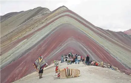  ?? Martin Mejia, The Associated Press ?? An Andean man rests with his llama while tourists take in the natural wonder of Rainbow Mountain in Pitumarca, Peru.