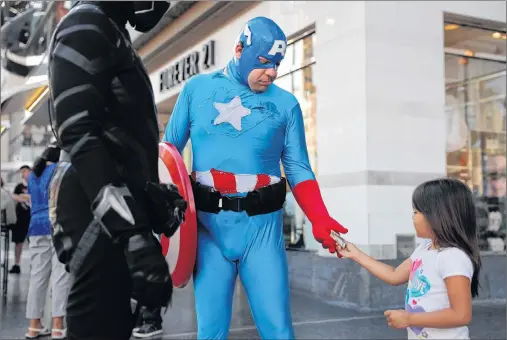  ?? AP PHOTO ?? A young tourist tips Justin Harrison, wearing a homemade Captain America costume, and Harrison’s roommate, Reginald Jackson in a Black Panther costume after taking pictures with them on Hollywood Boulevard in Los Angeles