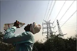  ?? MANISH SWARUP / AP ?? A worker quenches his thirst next to power lines as a heatwave continues to lash the capital, in New Delhi, India, on Monday. An unusually early and brutal heat wave is scorching parts of India, where acute power shortages are affecting millions as demand for electricit­y surges to record levels.