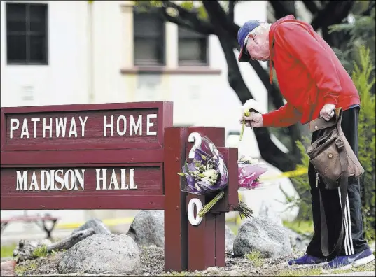  ?? Josh Edelson The Associated Press ?? Resident Tom Parkinson places flowers Saturday on a sign at The Pathway Home in Yountville, Calif. A hostage situation at the facility left four people dead, including the gunman.