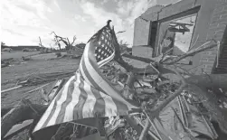  ?? GERALD HERBERT/AP ?? A flag flies Tuesday amid debris of destroyed homes in Mayfield, Ky., in the aftermath of tornadoes that tore through the region.