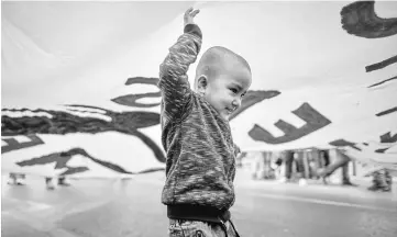  ??  ?? A child plays under a huge banner during a demonstrat­ion by Greek anti-fascist groups against the war in Syria and the European Union’s stance on refugees in Athens. — AFP photo