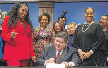  ?? TYLER PASCIAK LARIVIERE/SUN-TIMES ?? Gov. J.B. Pritzker on Monday signs a bill mandating paid leave for all Illinois workers starting in 2024. State Rep. Jehan Gordon-Booth is at left, while Senate Majority Leader Kimberly Lightford is at right, behind Pritzker.