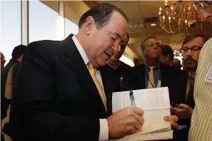  ?? AP Photo/Danny Johnston ?? Former Arkansas Gov. Mike Huckabee autographs a book after speaking Oct. 25, 2013, at a meeting of the Political Animals Club in Little Rock.
