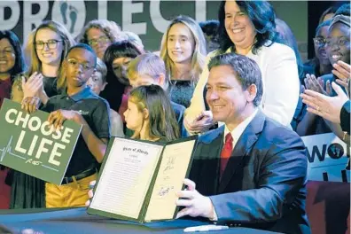  ?? JOHN RAOUX/AP ?? Gov. Ron DeSantis of Florida holds up a 15-week abortion ban law after signing it on April 14.
