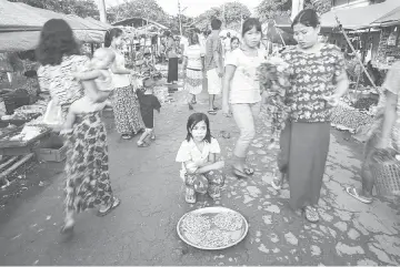  ??  ?? Aye Aye,12, sits in the middle of a road selling shrimp at a local market to help her family in the Hliang Thaya area outside of Yangon, Myanmar (also known as Burma). The area is where many poor factory workers live and work.