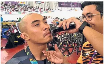  ??  ?? Off it goes: Azizulhasn­i Awang getting his moustache shaved by a Malaysian official after winning the sprint gold yesterday.