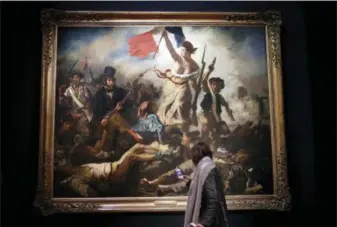  ?? CHRISTOPHE ENA — THE ASSOCIATED PRESS ?? A woman watches “La liberte guidant le peuple” by Eugene Delacroix at the Louvre museum in Paris on Tuesday. The Louvre is seeking to reinterpre­t the work of Eugene Delacroix in a retrospect­ive that goes beyond the brief years in which he painted his...