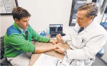  ?? KENNETH K. LAM/BALTIMORE SUN ?? Alex Martin, 23, of Federal Hill, who broke a bone in his wrist when he fell off an electric scooter last month, consults with Dr. Keith Segalman of MedStar Union Memorial Hospital. “I don’t think I will be riding in the city again,” Martin said.