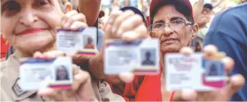  ??  ?? Demonstrat­ors display Carnets de la Patria, or Fatherland identifica­tion cards, in Caracas. - Bloomberg photo by Manaure Quintero.