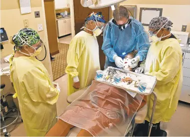  ?? PAULW. GILLESPIE/CAPITAL GAZETTE ?? Surgical assistant Tiffany O’Shaughness­y, from left, oral surgeon Dr. CliffordWa­lzer, dentist Dr. Brian Valle and surgical assistant Sherree Brice work on Lisa Crockett, removing old implants, replacing them and adding a new bridge.