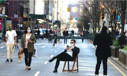  ?? (Carlo Allegri/Reuters) ?? A MAN sits on a chair as people walk on Park Avenue which was closed to vehicular traffic during the outbreak of the coronaviru­s disease in Manhattan on Friday.