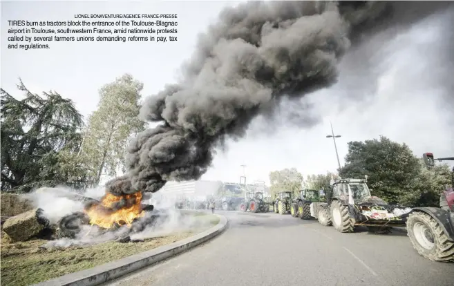  ?? LIONEL BONAVENTUR­E/AGENCE FRANCE-PRESSE ?? TIRES burn as tractors block the entrance of the Toulouse-Blagnac airport in Toulouse, southweste­rn France, amid nationwide protests called by several farmers unions demanding reforms in pay, tax and regulation­s.