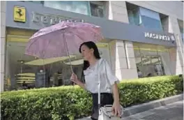  ?? — AFP ?? BEIJING: This picture taken on May 26, 2017 shows a woman using an umbrella as she walks past a Ferrari and Maserati store.