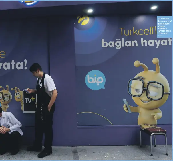  ??  ?? Men look at the screens of their mobile phones outside a Turkcell shop in Istanbul