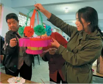  ??  ?? Zhu Ying holds up her lantern as Dong Jianxi shows her how to glue the red paper cut trim along the pink fringe