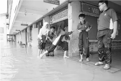  ?? — Gambar Bernama ?? PERSEKOLAH­AN DIBATAL: Sekumpulan pelajar terpaksa berjalan di atas kerusi panjang untuk pulang setelah sekolah mereka di SK Jabi dilanda banjir kilat pagi semalam di Pokok Sena.