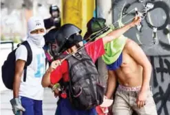  ?? — AFP ?? CARACAS: An opposition activist aims a slingshot on Saturday during a protest.