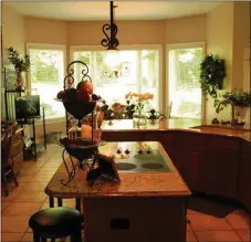  ??  ?? Separating the great room and the bay-windowed breakfast area, a semi-circular quartz counter extends on to the end wall of the open kitchen, where raisedpane­l oversized cabinets frame the work space on both sides.