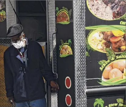  ?? Lori Van Buren / Times Union ?? An employee of Roy's Caribbean Restaurant stands by its food truck that is parked next to West Capitol Park steps in April 2020. Access to the Caribbean-based food was still plentiful during the pandemic.