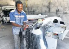  ??  ?? Odane Green washes a car bumper in preparatio­n for spraying.