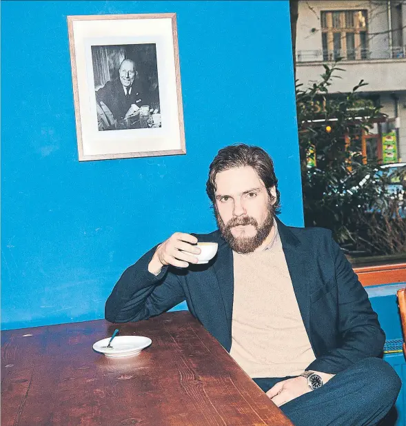  ??  ?? El intérprete hispanoale­mán Daniel Brühl, con barba debido a un rodaje, tomando un café bajo un retrato del actor Pepe Isbert, en el bar Gracia, qu
