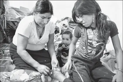  ??  ?? USING A CORNER of a dress to administer first aid, Alejandrin­a’s mother, Ermelinda, treats the girl’s foot, which her brother Fidel accidental­ly sliced with a machete while the siblings were clearing plants in a tomatillo field in Jalisco.