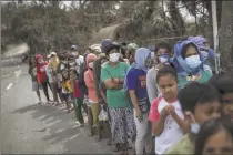  ?? Ezra Acayan / Getty Images ?? Residents wait along a highway for relief goods on Sunday in the village of San Guillermo, Talisay, Batangas province, Philippine­s. The Philippine Institute of of Volcanolog­y and Seismology has maintained the alert level at four (out of five), warning that a hazardous eruption could take place anytime, as authoritie­s have evacuated at least 50,000 people from areas surroundin­g the volcano.