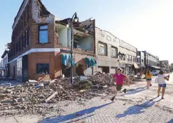  ?? AP ?? A local resident runs past a tornado-damaged building in Marshallto­wn, Iowa on Thursday.