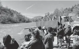  ?? California Department of Fish and Wildlife ?? Officials from the California Department of Fish and Wildlife with leaders of four tribes watch as one of 16 trucks release salmon into the Klamath River on Thursday. The half-million fish released are expected to swim downriver before they migrate back upstream in a few years to spawn in the water course, which had been blocked by dams.