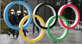  ?? ASSOCIATED PRESS FILE PHOTO ?? People wearing masks walk past the Olympic rings near the New National Stadium in Tokyo.