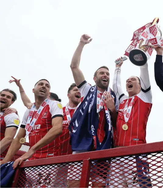  ??  ?? Cheltenham Town manager Michael Duff and the players celebrate with the trophy as League Two champions outside the Jonny Rocks Stadium