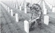  ?? AP ?? On Thursday, Army Cpl. Matthew Munie, of Jackson, Mich., and a member of the 3d U.S. Infantry Regiment also known as The Old Guard, placed flags in front of a headstone for “Flags-In” at Arlington National Cemetery in Arlington to honor the nation’s fallen military heroes.