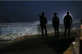  ?? MARCO UGARTE — THE ASSOCIATED PRESS ?? Residents stand on a hill before barriers, wrapped in concertina wire, separating Mexico and the United States, where the border meets the Pacific Ocean, in Tijuana, Mexico, Saturday. Many of the nearly 3,000 migrants have reached the border with California. The mayor has called the migrants’ arrival an “avalanche” that the city is ill-prepared to handle.