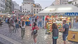  ?? (AFP) ?? People walk by a kiosk at Monastirak­i Square, an area popular with tourists, in Athens on Friday