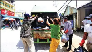  ?? HEAN RANGSEY ?? Officers and residents throw rubbish into a truck in the capital’s Meanchey district.