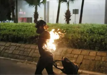  ?? Kin Cheung/Associated Press ?? A protester’s back catches fire after attempting to throw a Molotov cocktail Saturday in Hong Kong. In yet another day of clashes, protesters threw bricks, set fires and burned a Chinese flag, and police fired pepper spray.