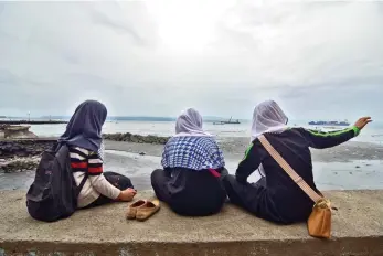  ?? MACKY LIM ?? BREAK TIME. Young Muslim girls pass the time away at Magsaysay Park’s seawall.