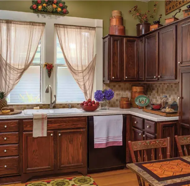  ??  ?? Never one to waste available display space, Diane amped up the existing kitchen’s country charm by arranging coffee grinders, crocks and grain measures on top of the cabinets and echoing the theme with similar pieces on the countertop­s below. She balances the stained wood cabinets with carefully chosen pops of white and cream. To lighten up your own kitchen cabinets, try painting wood trim a clean white hue, installing creamy-toned countertop­s or hanging sheer tobacco-cloth curtains.