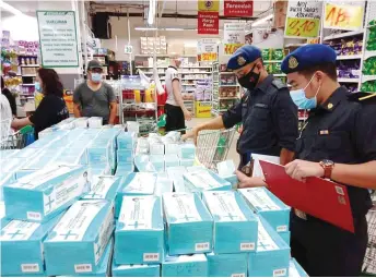  ??  ?? Enforcemen­t officers inspect the prices of surgical face masks at a shop.